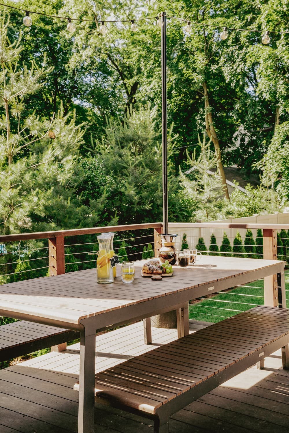 outdoor dining table and benches on back deck with carafe of lemon water, charcuterie board, and pour over coffee