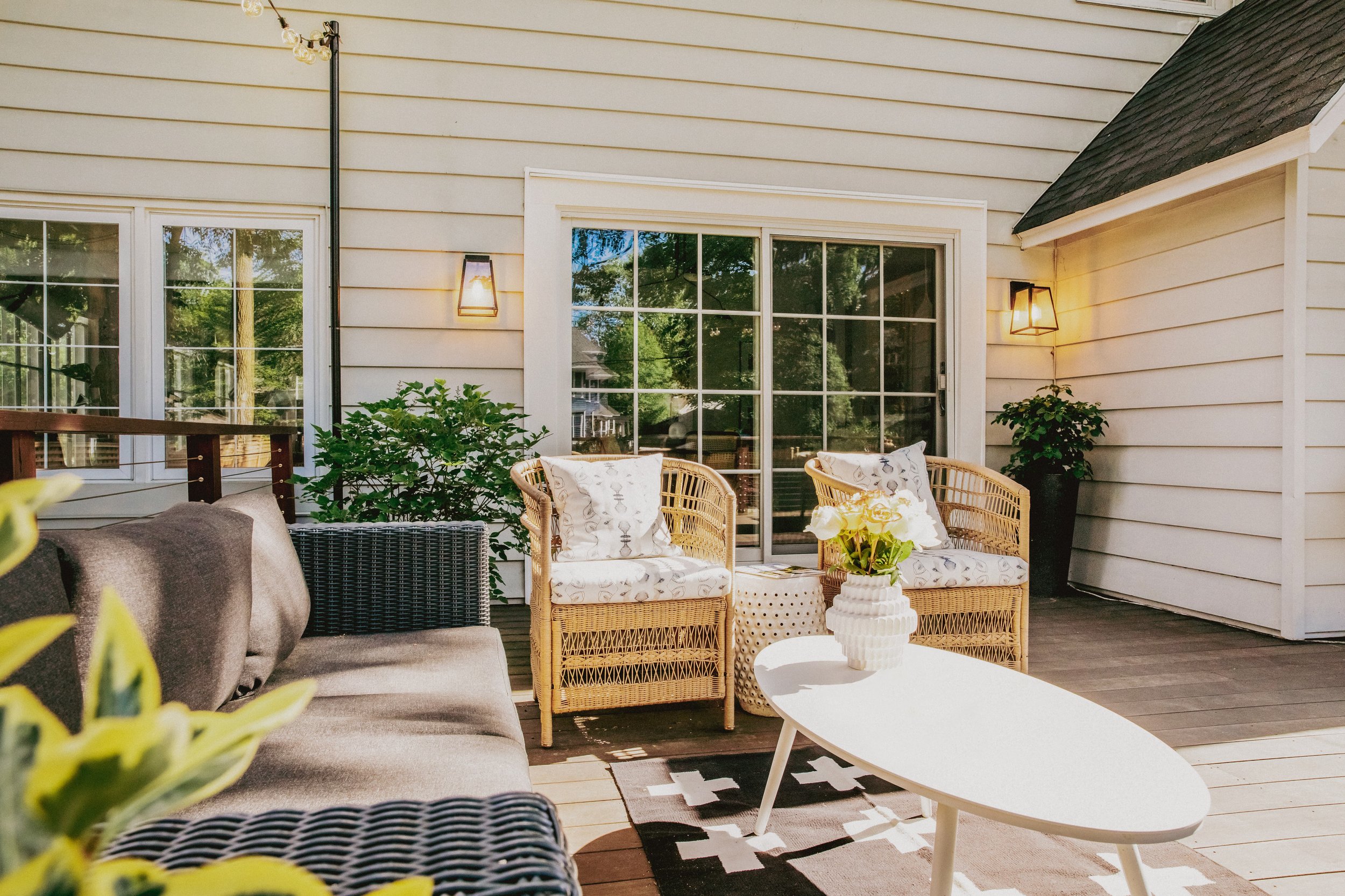 seating area on back deck with modern white coffee table, two rattan chairs, and black wicker outdoor sofa