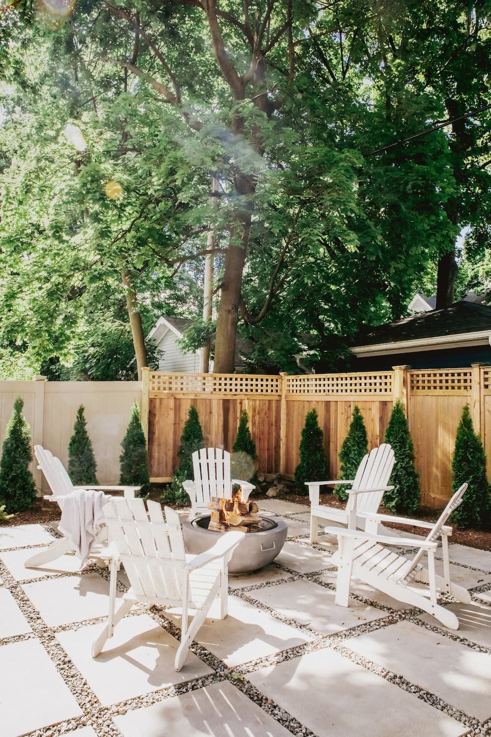 tall view of corner of yard with fire pit patio, privacy fence, and hedges