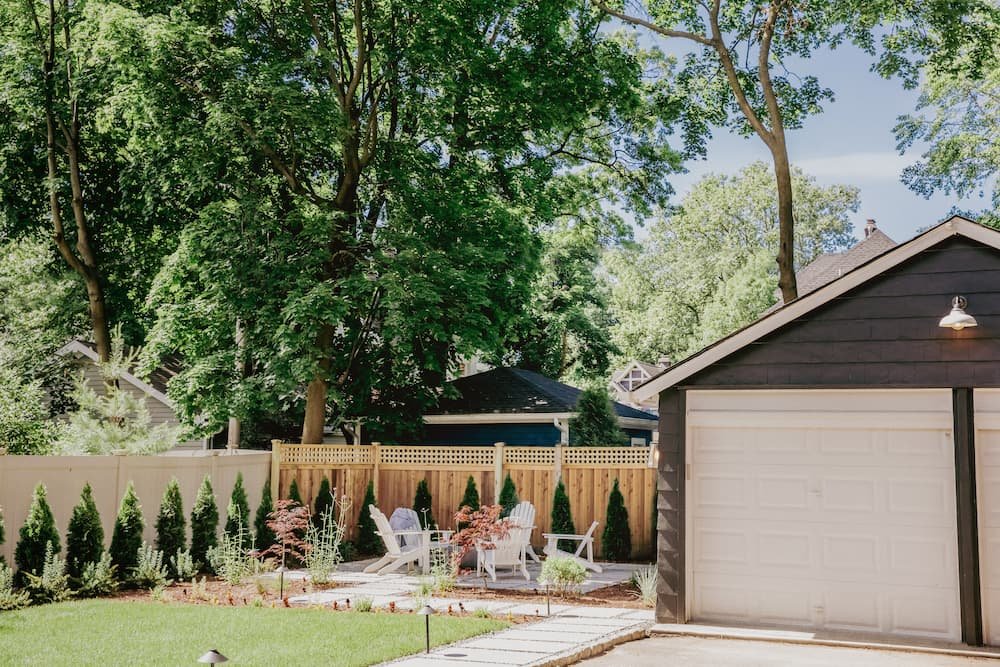 wide view of backyard from the home with two door garage, walkway, fire pit area, and privacy fence and hedges