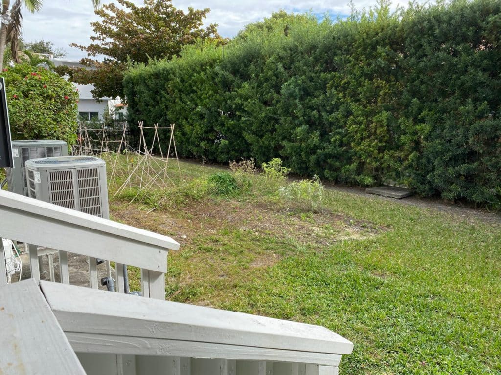 Before image view of backyard with grass, dirt, and A/C units