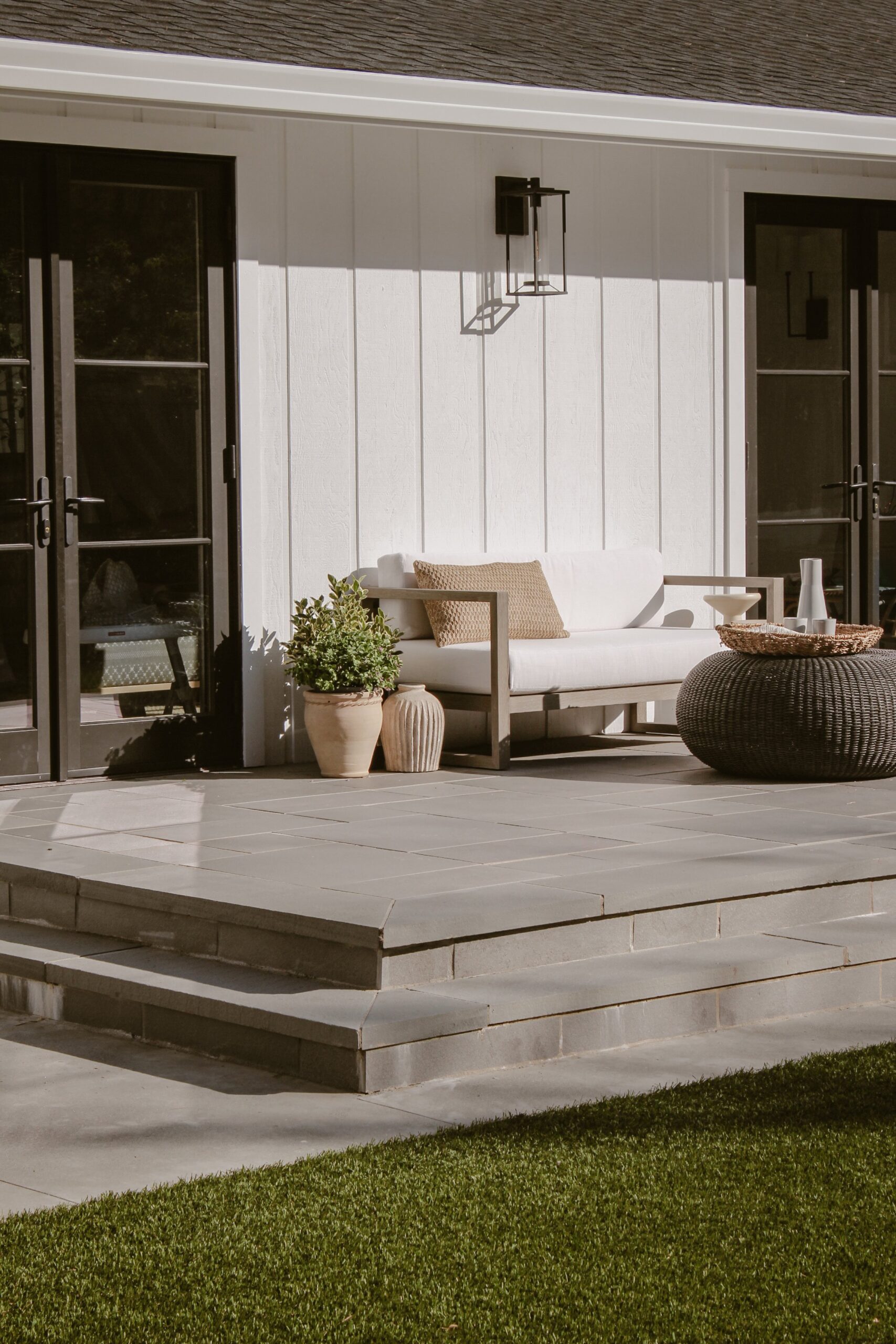 Close up of paver patio steps at back of home with outdoor sofa and wall-mounted light