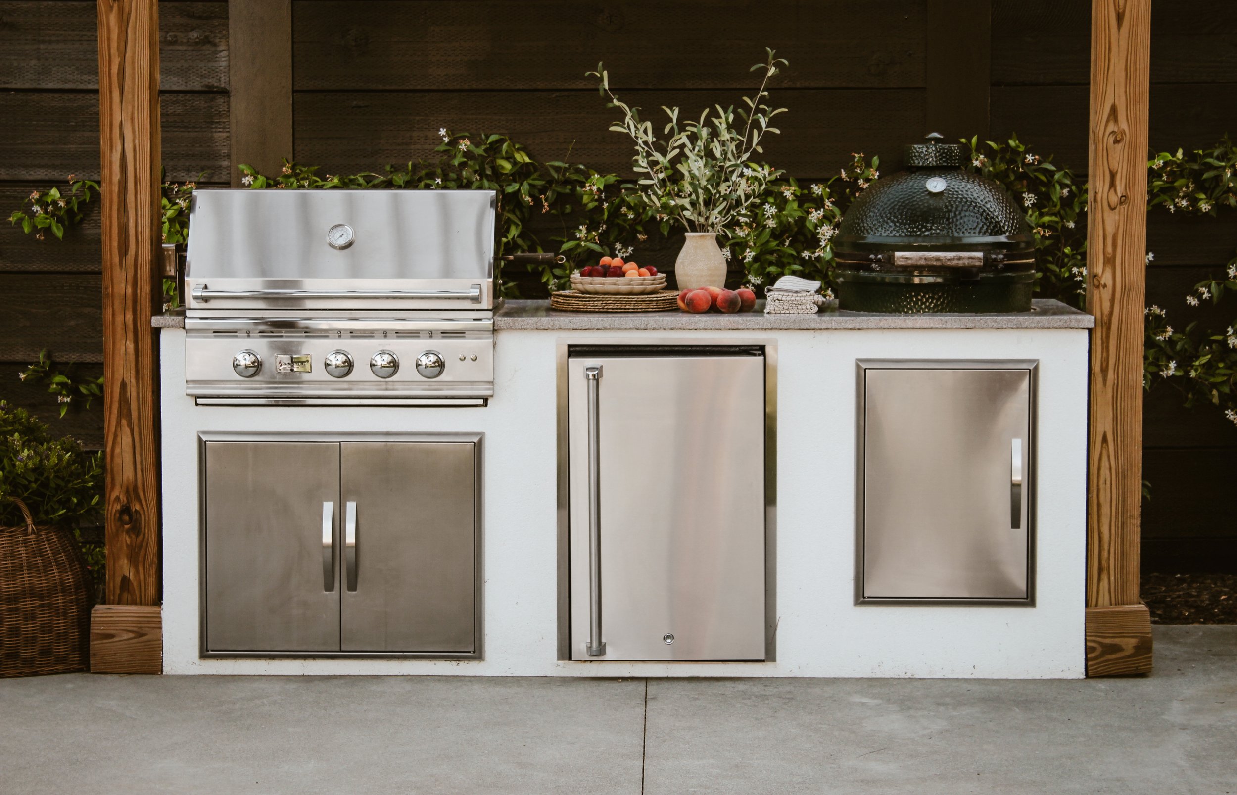 Close up of outdoor kitchen with stainless grill, refrigerator, and smoker
