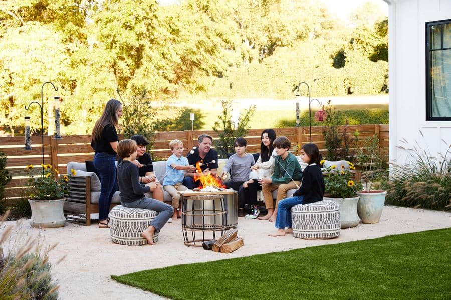 Zoë, Matt and their family enjoy s'mores around their Solo Stove. The firepit area features container plants, pouf seating, couch, decomposed granite and four-foot horizontal fencing.