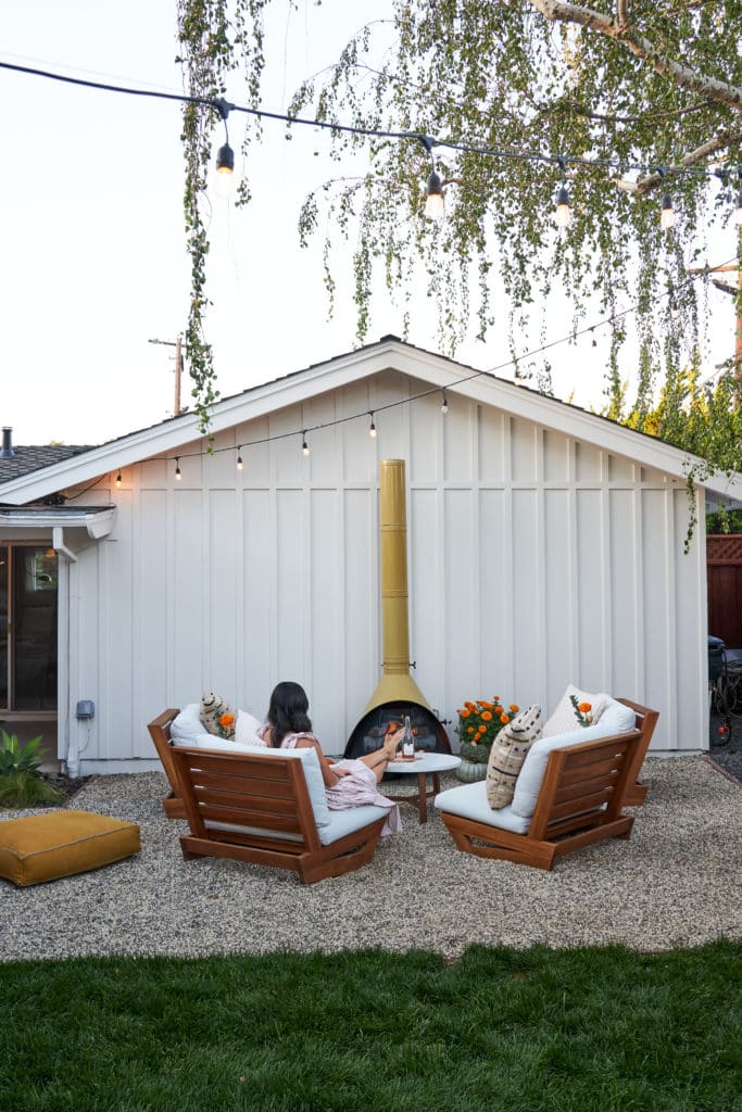 Kristy in an outdoor lounge chair with feet propped on a coffee table in front of their midcentury modern outdoor fireplace