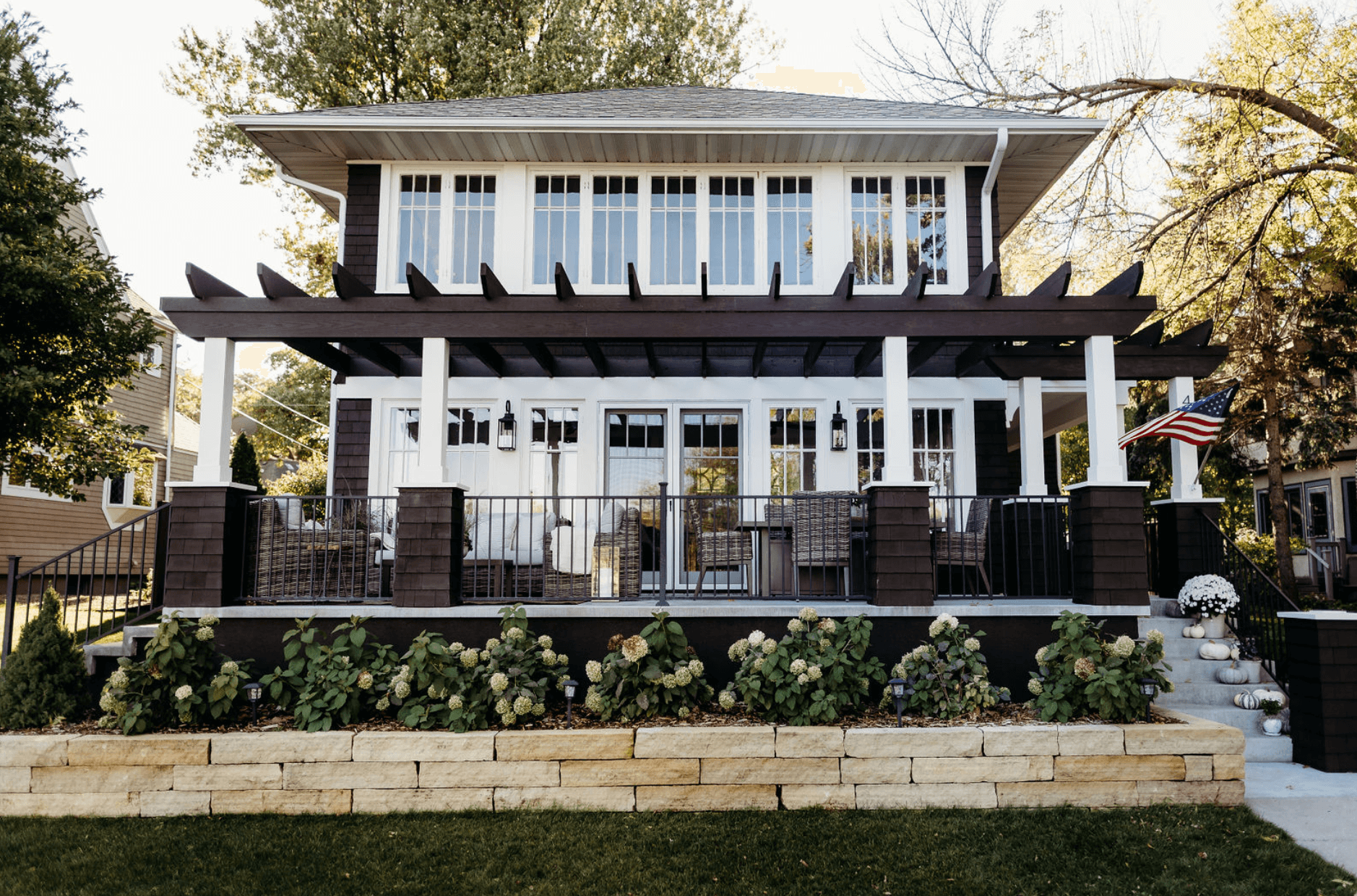 a house with a large deck in the front yard and a row of white hydrangeas
